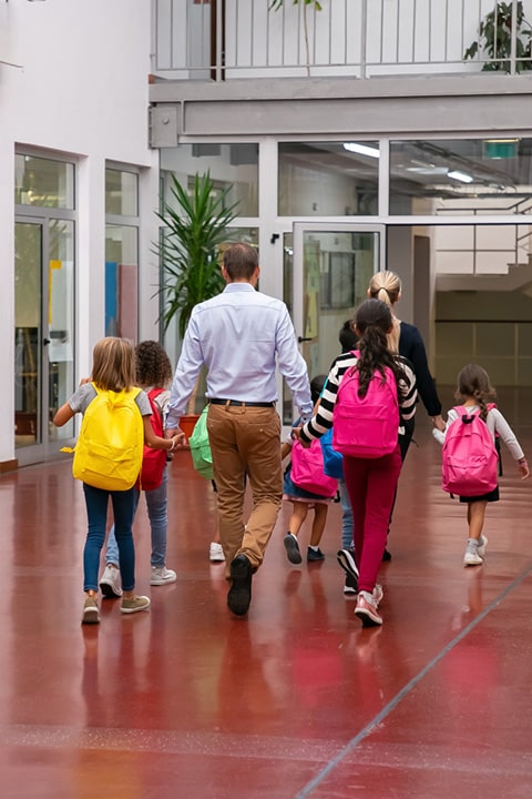 schoolkids-with-bright-backpacks-walking-through-school-hallway-holding-hands-teachers
