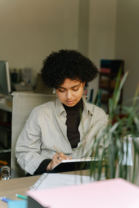 a-woman-in-striped-long-sleeves-writing-on-notebook